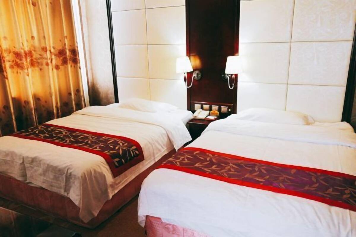 Une chambre d’hôtel avec deux lits, chacun recouvert d’une couverture rouge et blanche, dotée d’une tête de lit en bois et d’une table de chevet avec un téléphone.