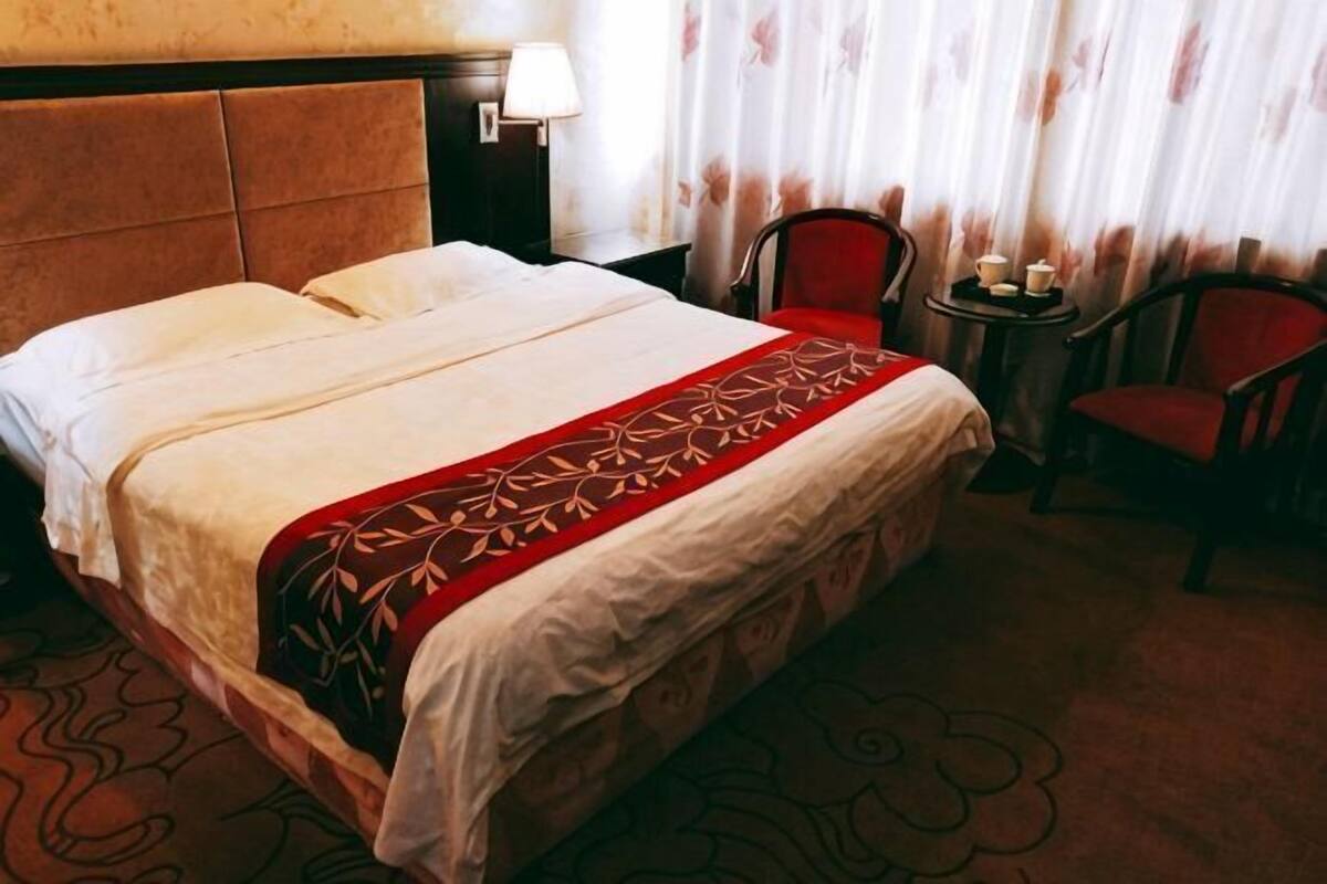 Une chambre d’hôtel avec un lit, une chaise, une petite table avec une lampe et des rideaux.
