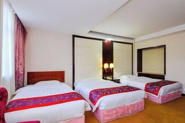 A hotel room with three beds, a wooden headboard, a large mirror, and a window with curtains.