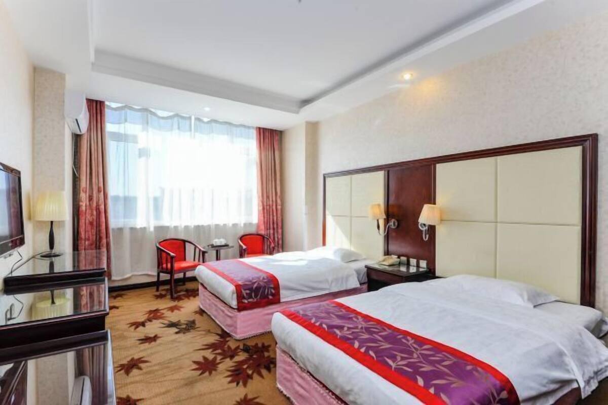 Une chambre d’hôtel avec deux lits, un bureau, une chaise, une télévision et une fenêtre avec des rideaux.
