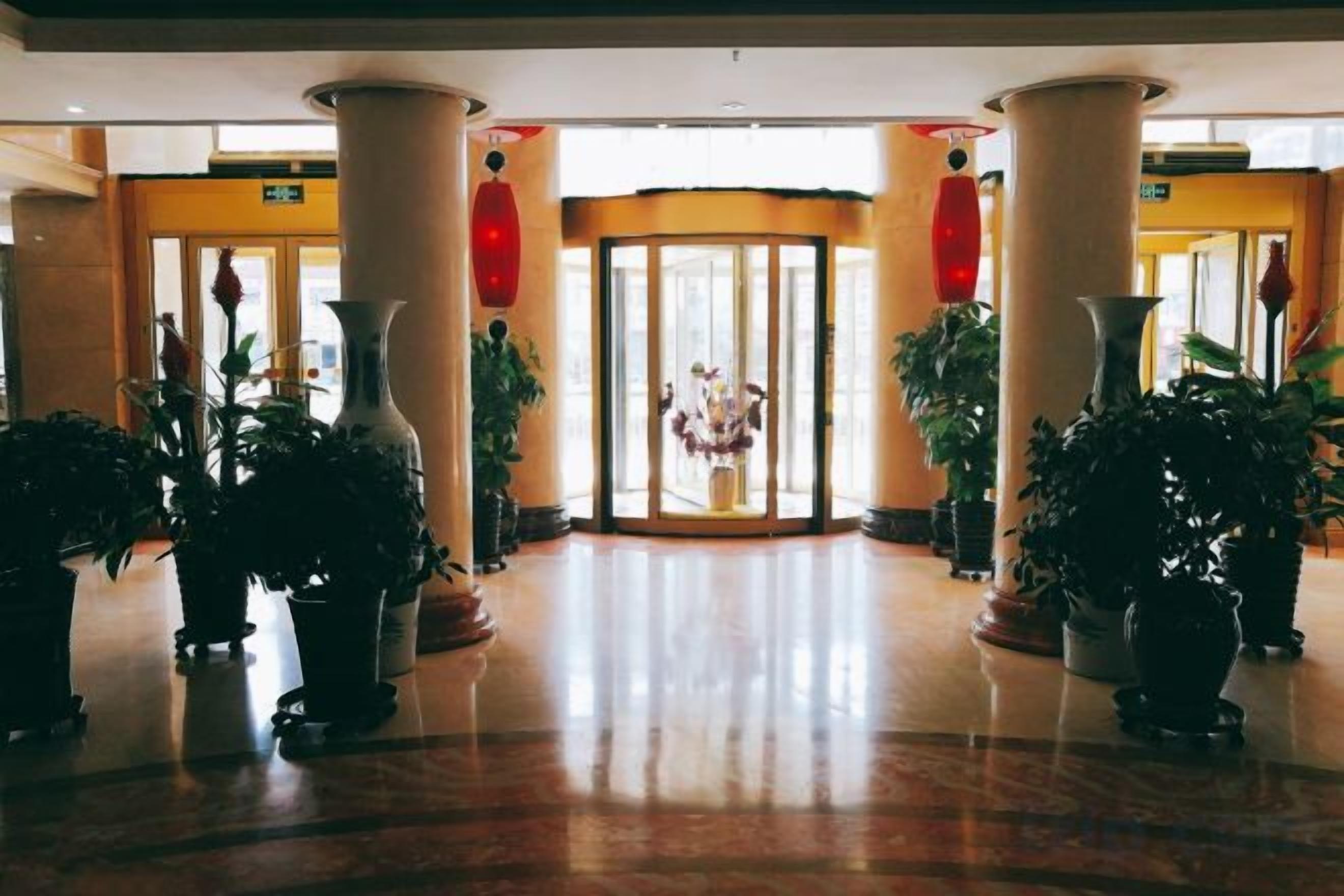 Un hall d’hôtel avec un sol en marbre, de grandes colonnes, des plantes en pot et une entrée avec une porte en verre.