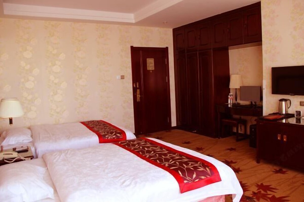 A hotel room with two beds, a desk, a chair, a television, and a wardrobe.