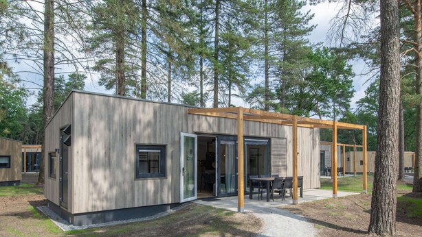 A modern cabin with a wooden exterior, large sliding glass doors, and a covered outdoor seating area. - Chalet in Eindhoven Near Green Forests (Mierlo)