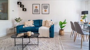 Un saló modern amb un sofà blau, una taula de centre i una zona de menjador amb cadires i taula.