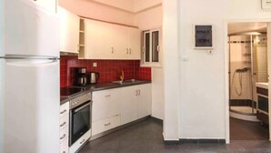 A compact kitchen with white cabinets, a red-tiled backsplash, a built-in oven, and a coffee maker. - Perfect choice for your stay in central Athens (Athina)