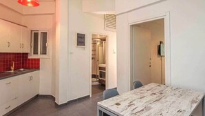 A compact kitchen with white cabinets, a red backsplash, and a dining area with a rustic table. - Perfect choice for your stay in central Athens (Athina)