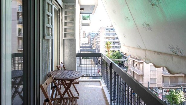 A balcony with a table and chairs, a view of the street below, and a building with balconies in the background. - Perfect choice for your stay in central Athens (Athina)