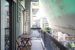 Een balkon met een tafel en stoelen, uitzicht op de straat hieronder, en een gebouw met balkons op de achtergrond.