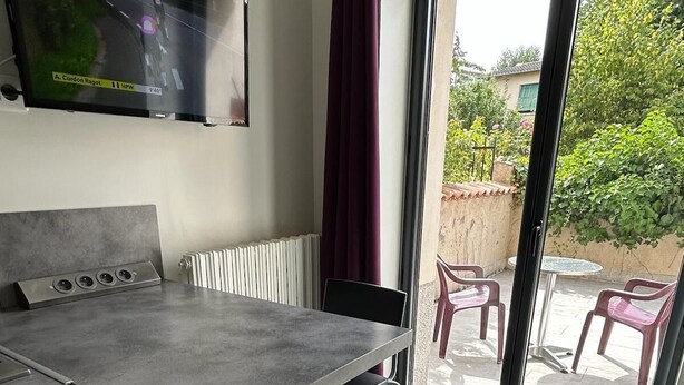 Une chambre moderne dotée d’une grande fenêtre, d’un téléviseur à écran plat fixé au mur, d’une table à manger avec des chaises et d’un radiateur.