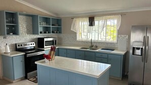 A kitchen with blue cabinets, a stainless steel refrigerator, a microwave, and a sink. - Hope Winds - by Zenbreak (Providence)