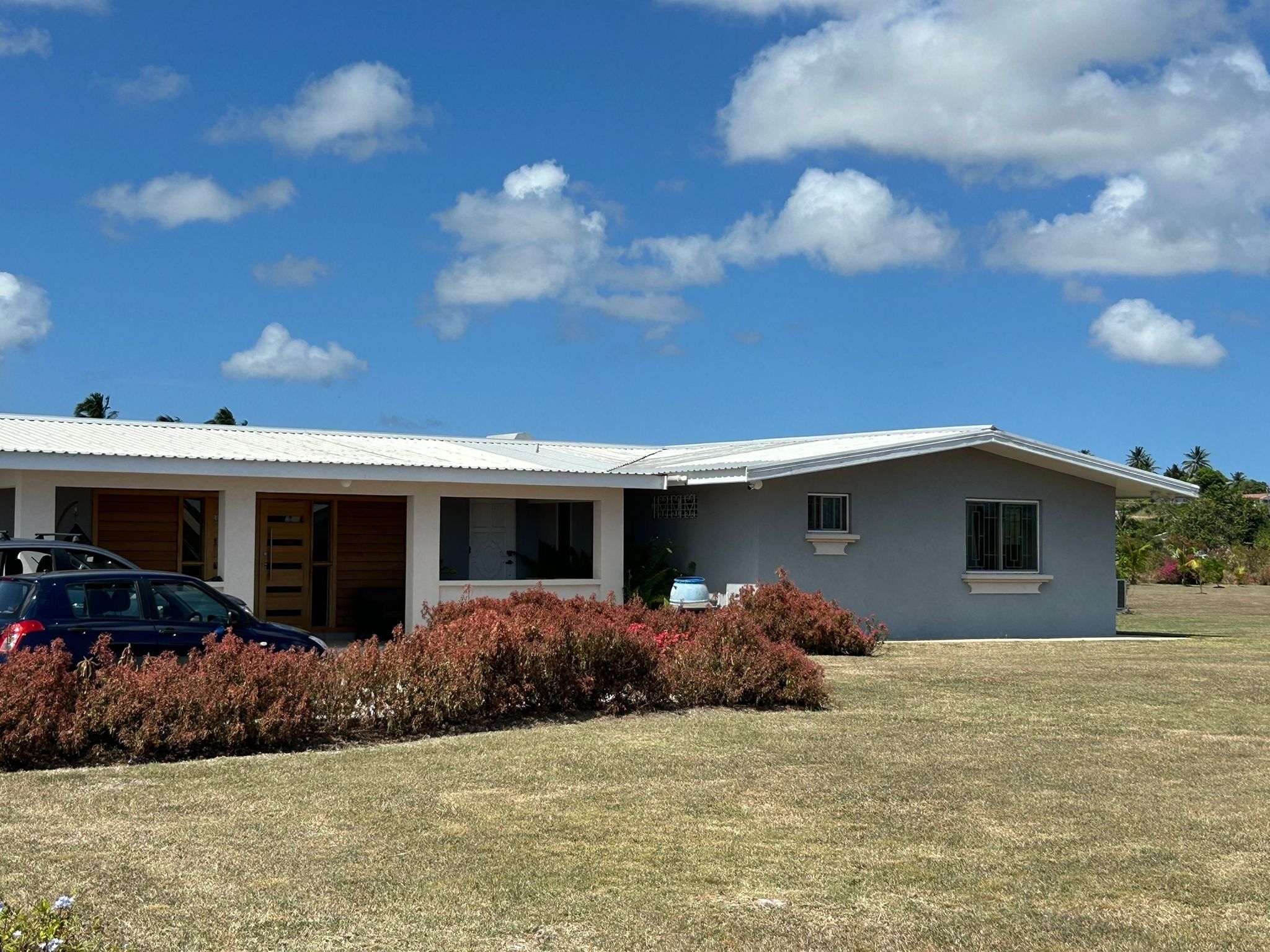 A single-story house with a flat roof, a covered porch, and a front yard with a car parked in the driveway.