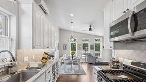 Een moderne keuken met witte kasten, roestvrijstalen apparatuur en een eethoek met een kroonluchter.