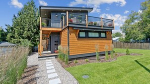 Een modern huis met twee verdiepingen, een balkon, houten bekleding en een verzorgd gazon.