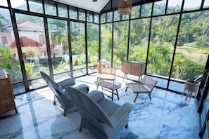A spacious room with large windows, a seating area with chairs, a small table, and a hanging light fixture.