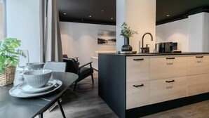 A modern kitchen with a central island, a dining area with a table and chairs, and a view of the cityscape through large windows. - B2 - Two Bedroom Apartment with Balcony (Reykjavík)
