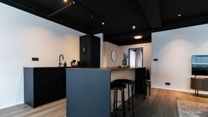 Uma cozinha moderna com uma ilha central, banquetas, uma pia e uma televisão.