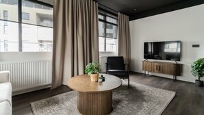 Un salon moderne avec une table ronde en bois, une chaise noire, un téléviseur et une plante en pot.