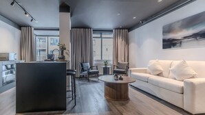 Un salon moderne comprenant un canapé, une table basse et un coin cuisine avec un réfrigérateur et une bouilloire.