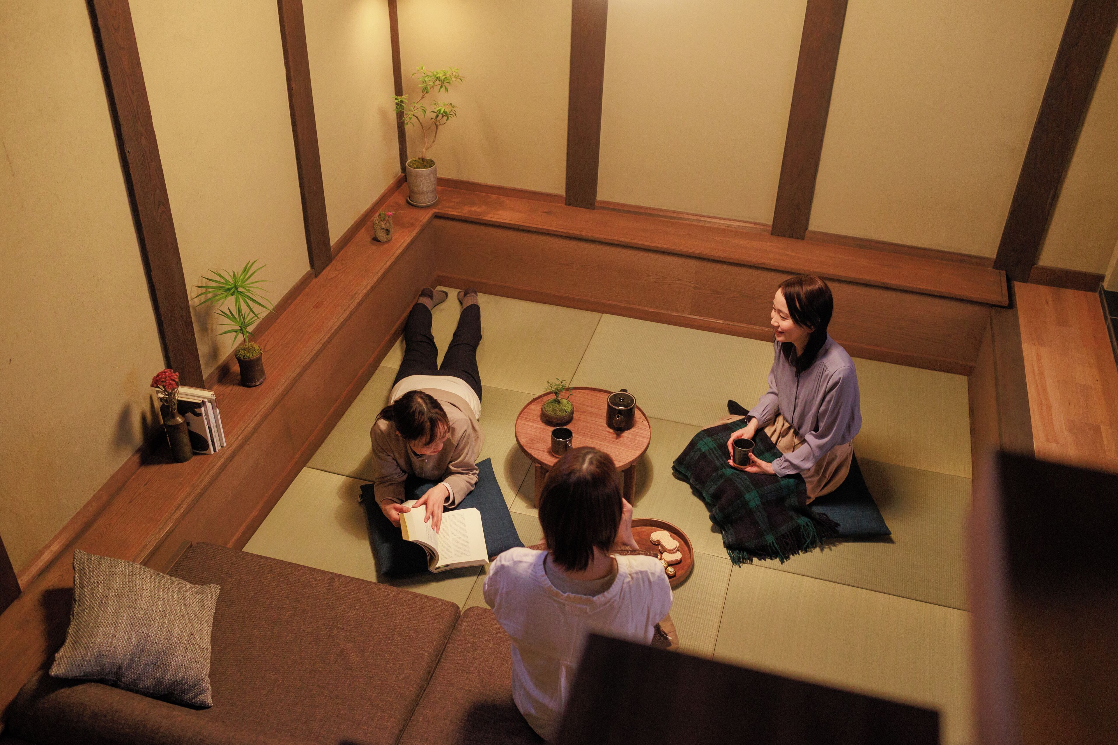 A tatami mat room with a low wooden table, cushions, and a small potted plant.