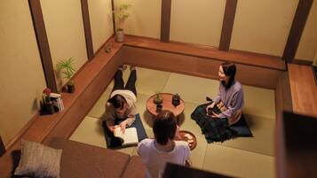 A tatami mat room with a low wooden table, cushions, and a small potted plant.