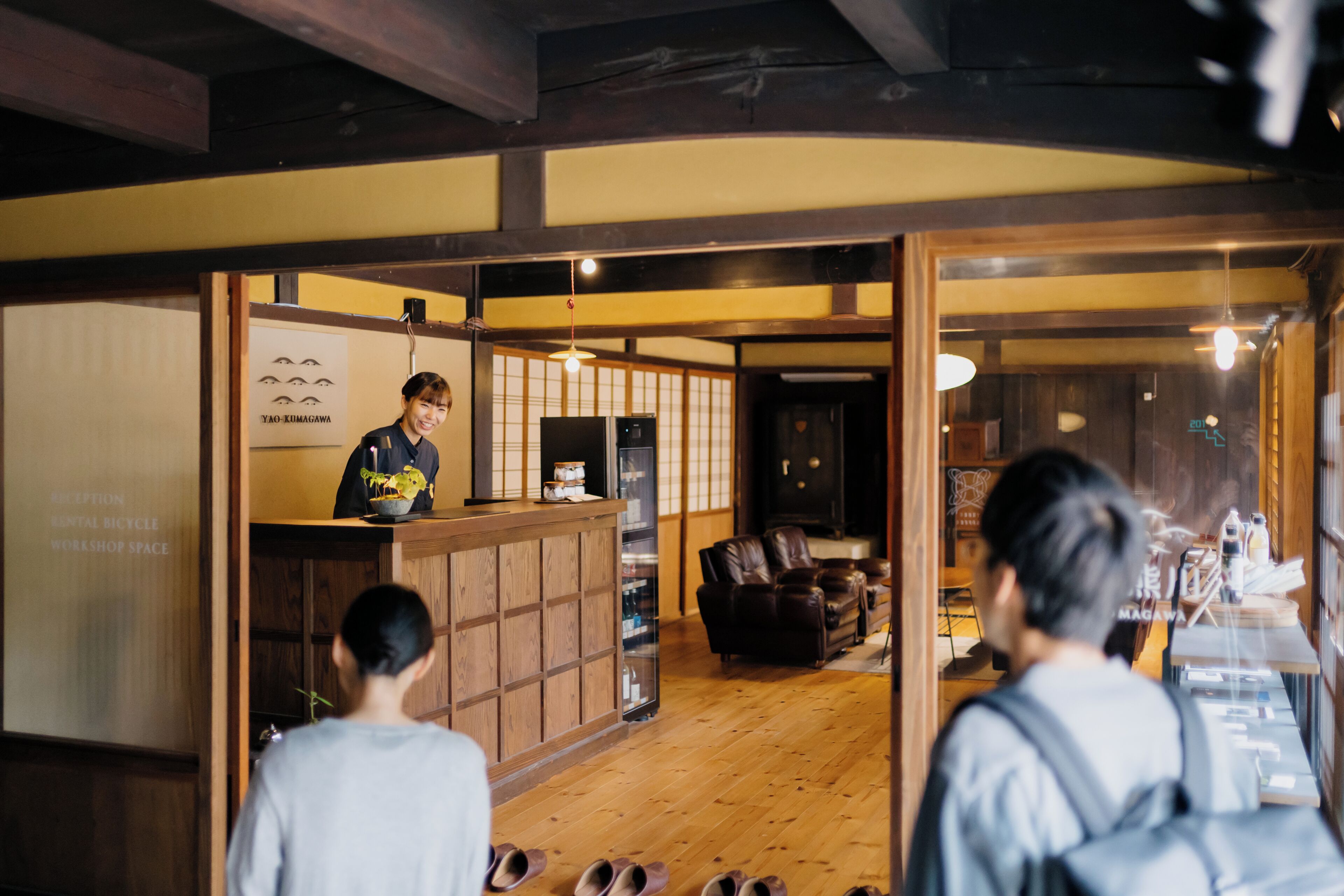 Un espace d’accueil comprenant un comptoir en bois, un bureau de réception et un coin salon avec un canapé et des fauteuils.