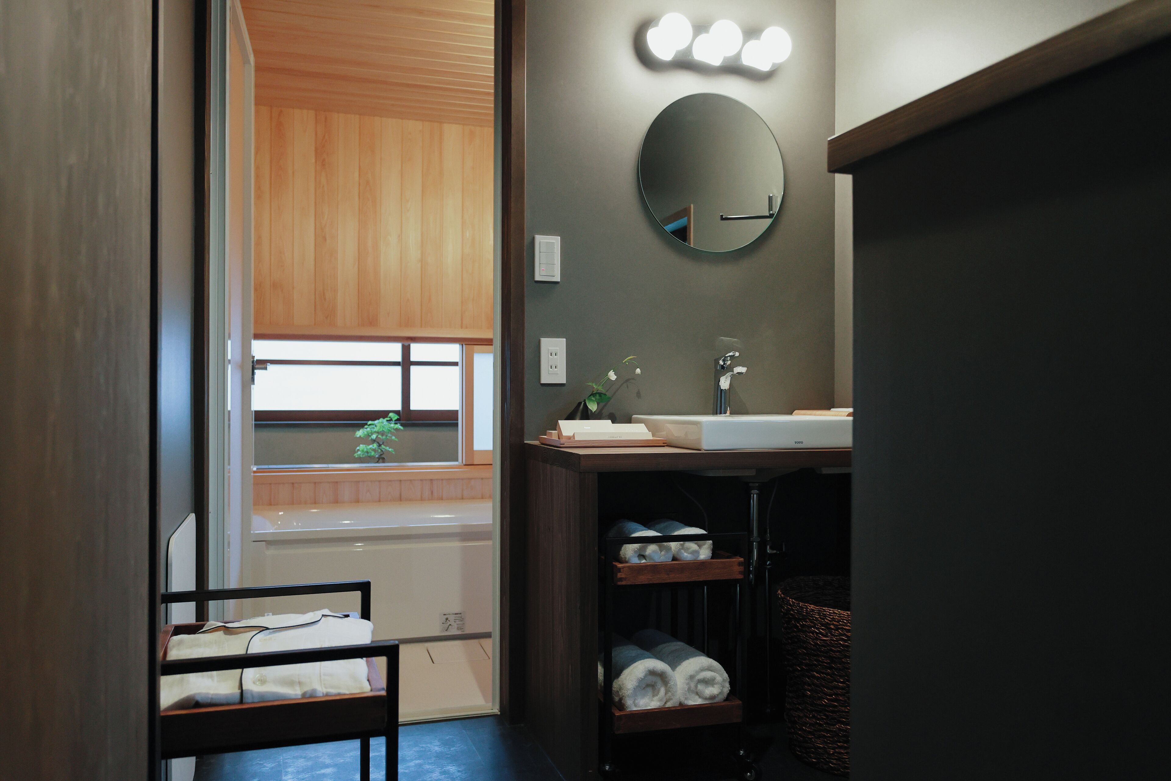 Un baño con tocador de madera, un espejo redondo y una ventana con persianas.