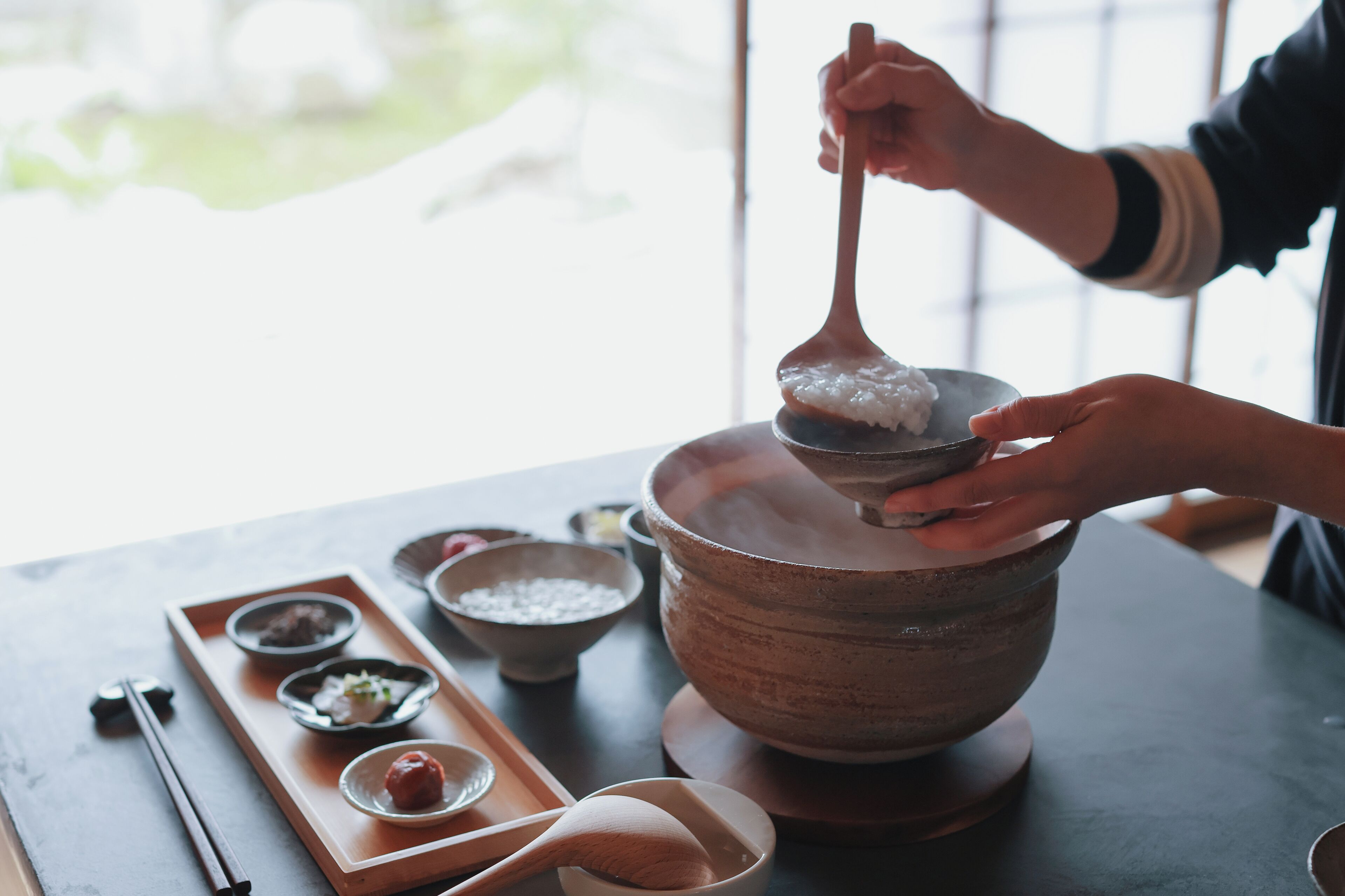 Une personne servant du riz dans un grand bol, sur une table où se trouvent divers plats et ustensiles.