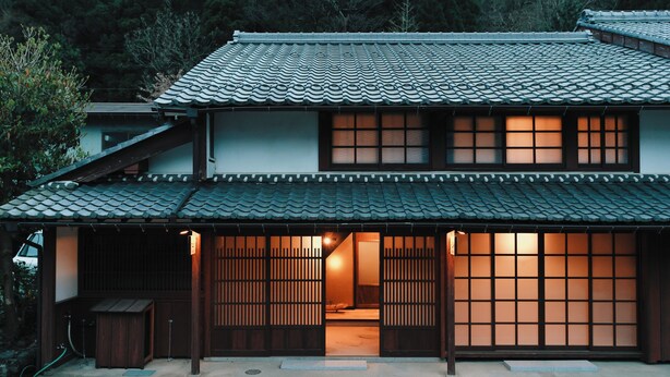 A traditional Japanese house with a tiled roof, sliding doors, and a visible interior with a light source. - 八百熊川 Yao-Kumagawa (Wakasa)