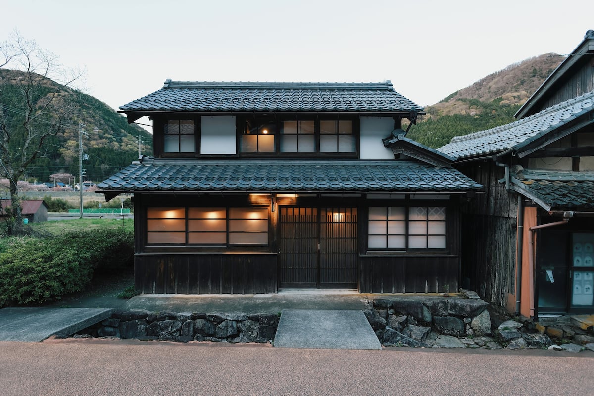 Una casa japonesa tradicional con techo de tejas, entrada de madera y un camino de piedra que lleva a la puerta.