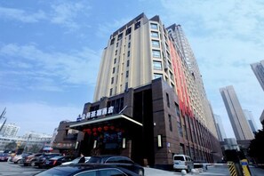 Un hôtel à plusieurs étages, doté d’une entrée imposante et d’une bande verticale rouge qui souligne la façade.