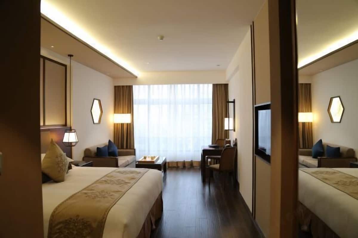 Habitación de hotel con dos camas, un escritorio, una silla, un televisor y un amplio ventanal con cortinas.
