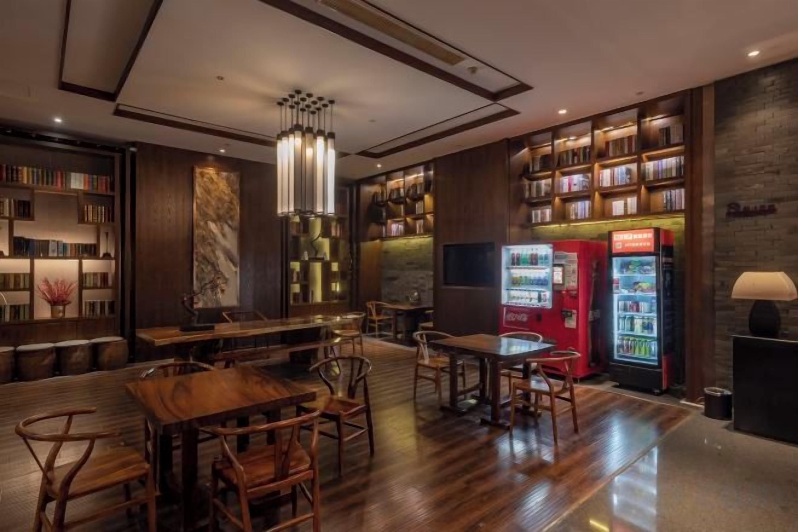 A library with bookshelves, tables, chairs, a red vending machine, and a marble wall.
