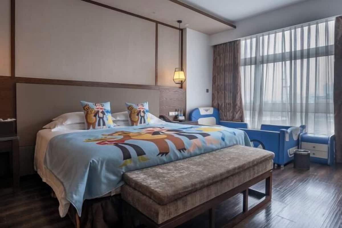 Una habitación de hotel con cama, un banco, un escritorio y una ventana con cortinas.