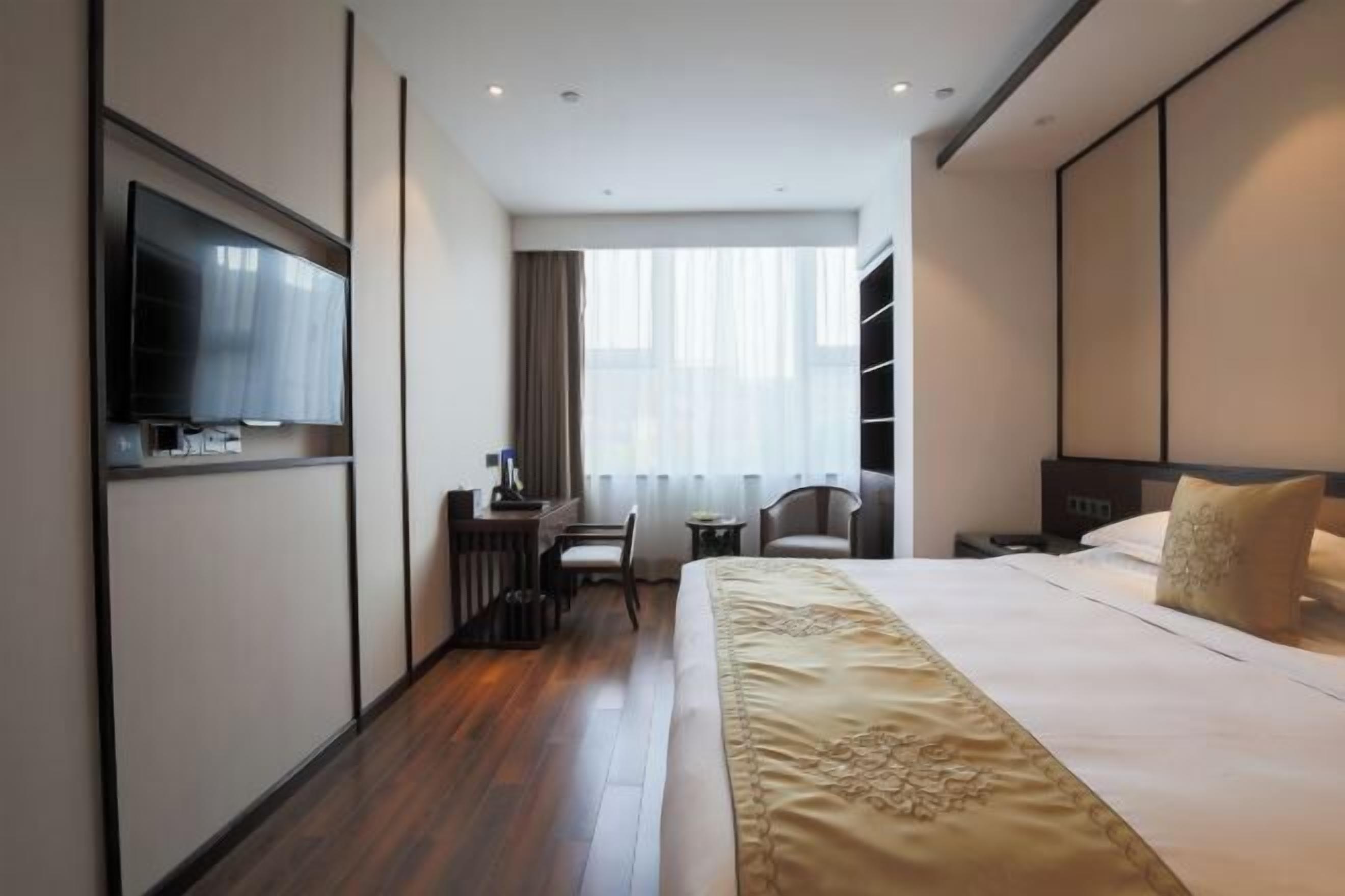 A hotel room with a large bed, a desk with a chair, a television, and a window with curtains.