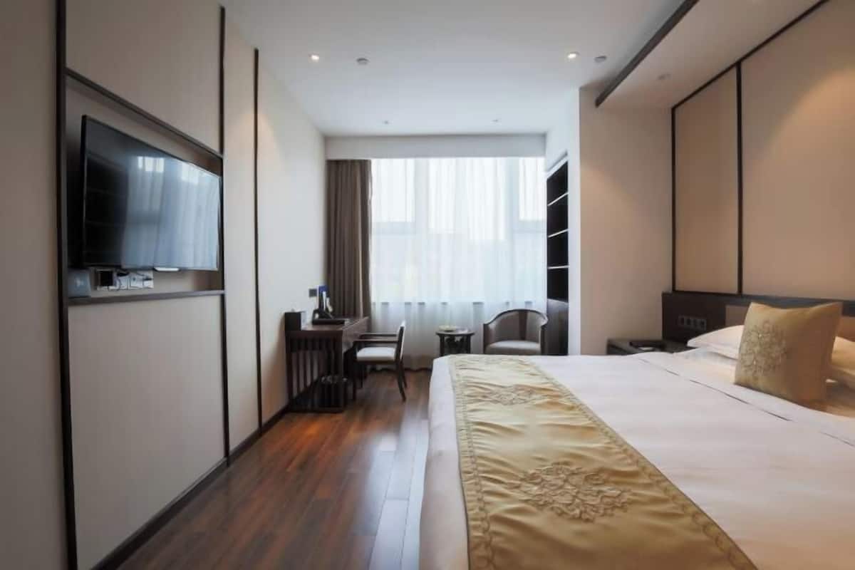 A hotel room with a large bed, a desk with a chair, a television, and a window with curtains.