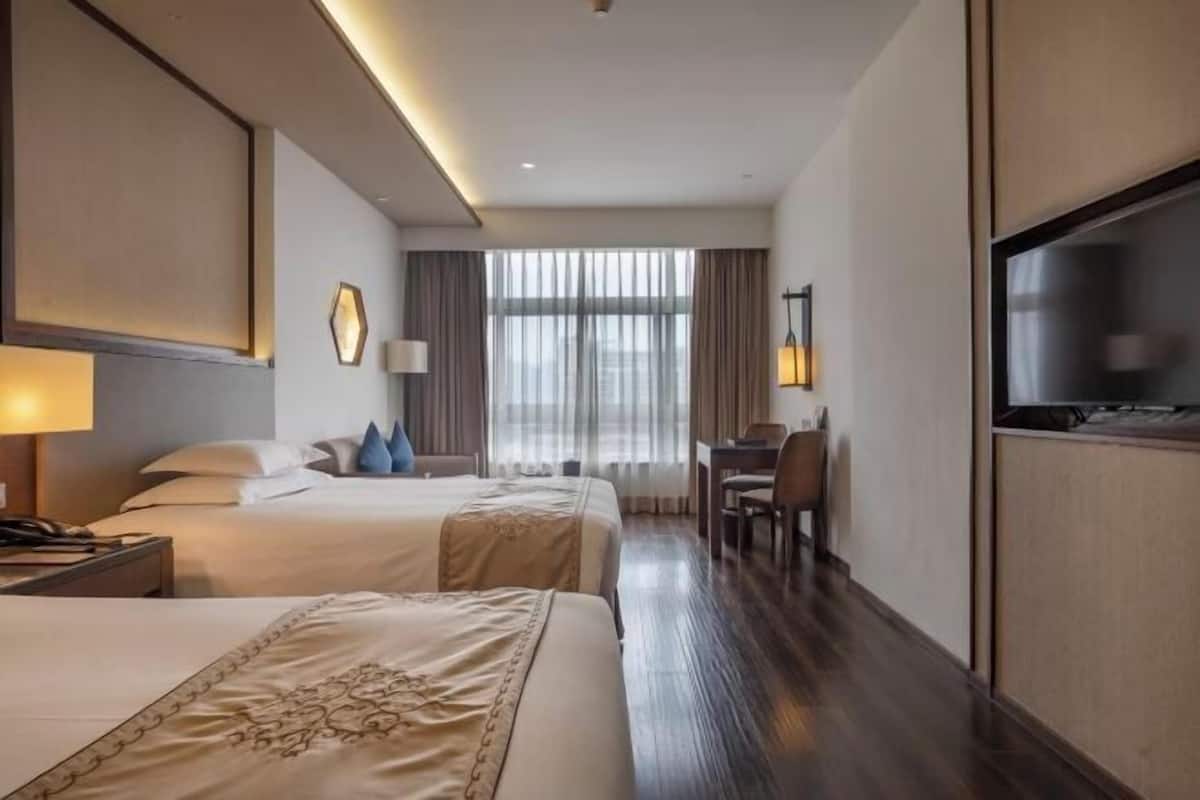 Habitación de hotel con dos camas, un escritorio, una silla, un televisor y un ventanal con cortinas.