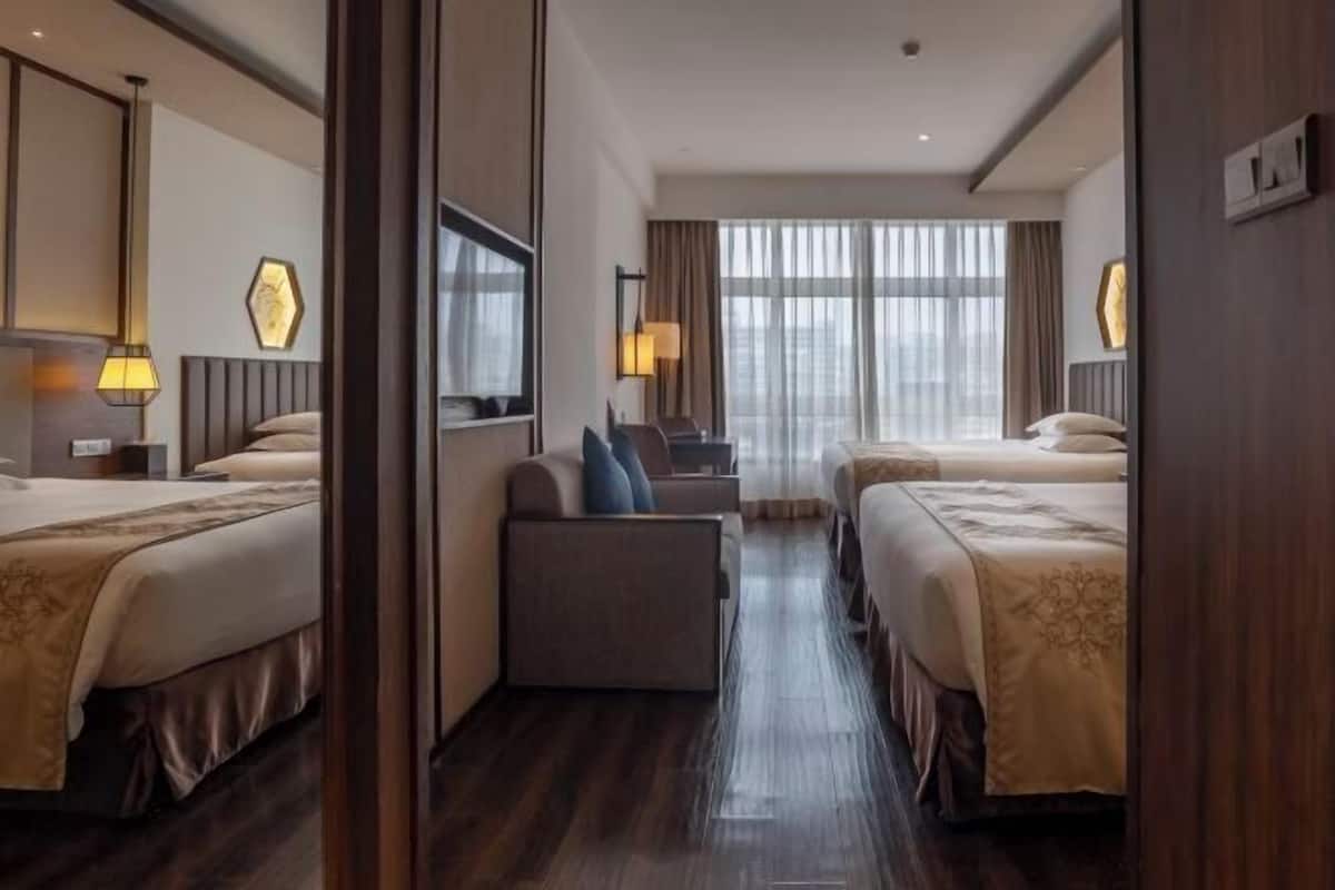 Habitación de hotel con dos camas, un sofá, un escritorio y un ventanal con cortinas.