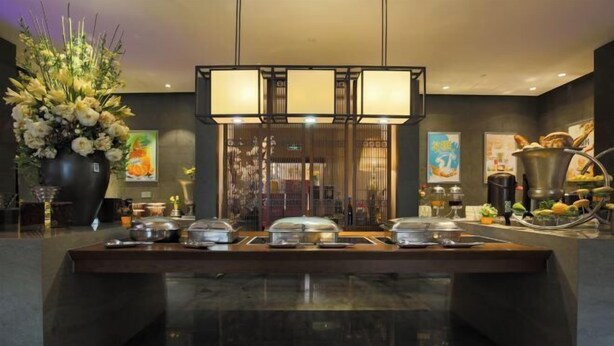A buffet setup with covered food stations, a large vase of flowers, and artwork on the walls. - Jinke Saint Hotel (Wuxi)