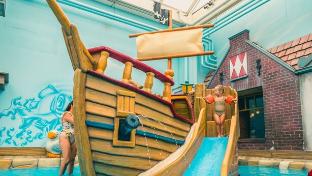 A wooden pirate ship slide in a swimming pool area with a mural of fish and a brick building with a red 'M' logo. - Modern Eco-villa Near the Veluwemeer (Biddinghuizen)
