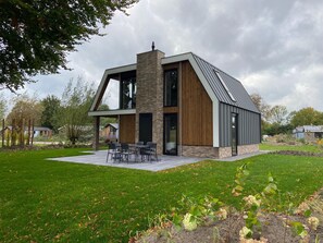 A modern two-story house with a large patio, a chimney, and a view of the surrounding area.
