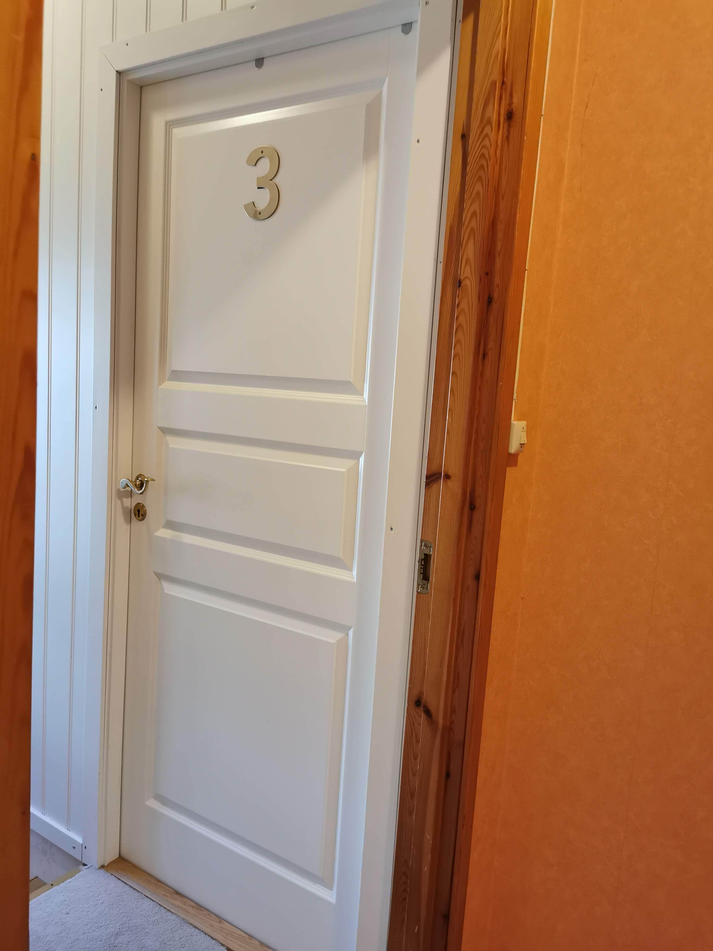 Eine weiße Tür mit der Nummer 3, einem Messing-Drücker und einem hölzernen Türrahmen.