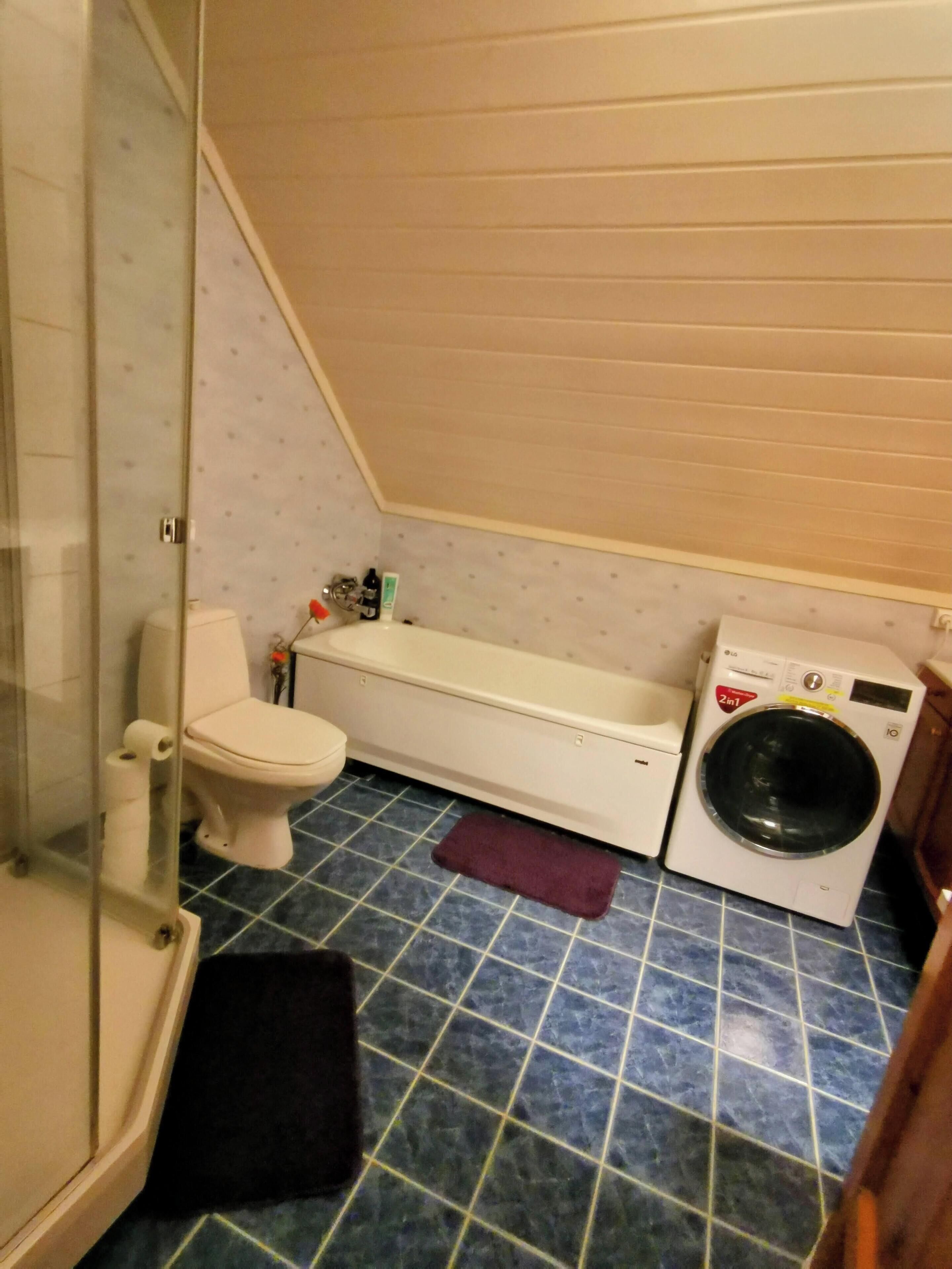 Un bany compacte amb vàter, un banc, una rentadora i un plat de dutxa amb envà.