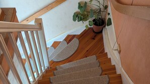 Una escalera de madera con barandilla, una planta en maceta y un felpudo en la parte inferior.