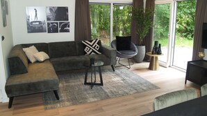 Un salon moderne avec un canapé d’angle, une table basse ronde, un fauteuil gris et un téléviseur.