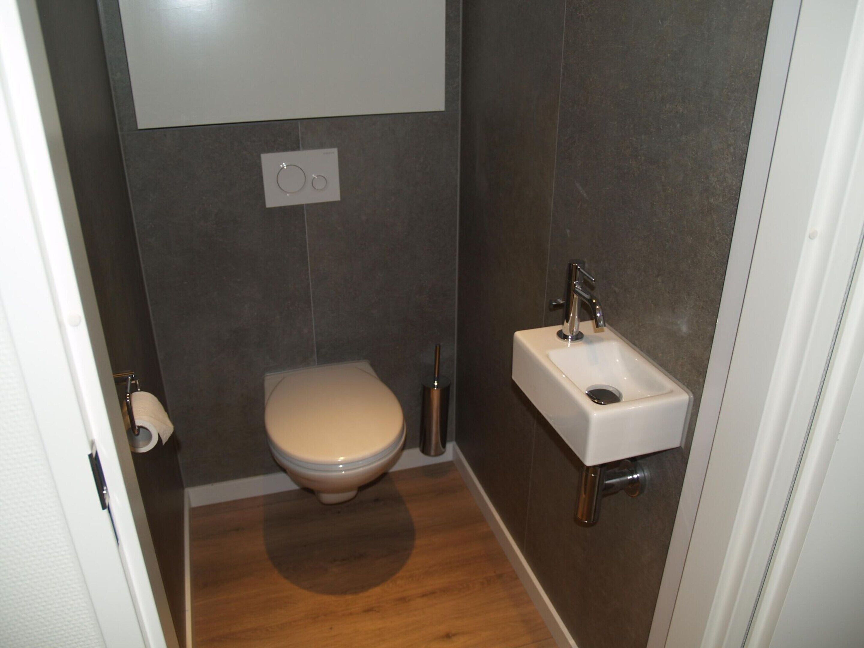 A small, modern bathroom with a toilet, a sink, and a toilet paper holder.