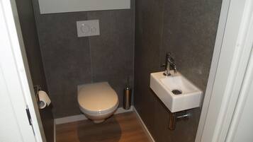 A small, modern bathroom with a toilet, a sink, and a toilet paper holder.