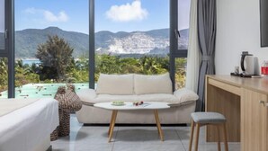 A modern hotel room with a large window offering a view of a mountainous landscape and a beach. - Here Nashan Nahai Surfing Seaview Homestay (Sanya Wuzhizhou Island Houhai Bay Branch) (Sanya)