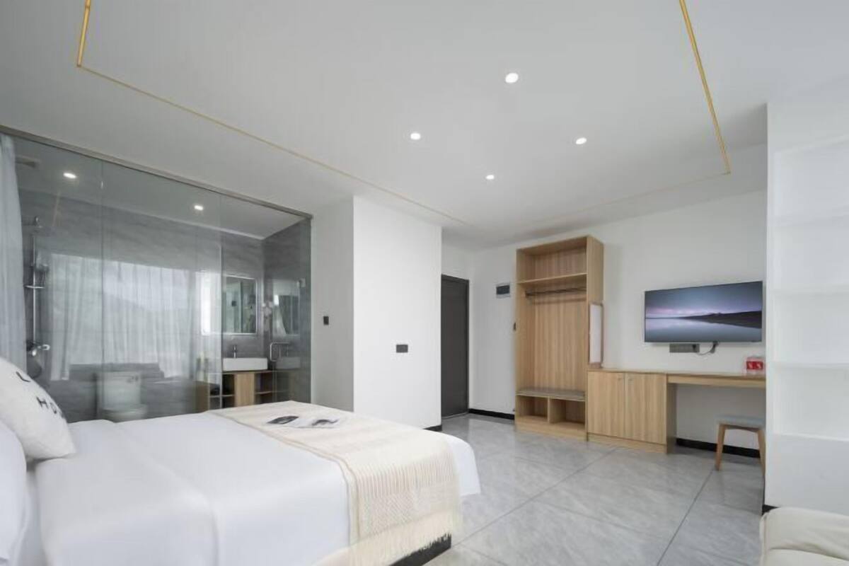 Une chambre d’hôtel moderne avec un grand lit, une douche en verre, un bureau en bois et un téléviseur fixé au mur.