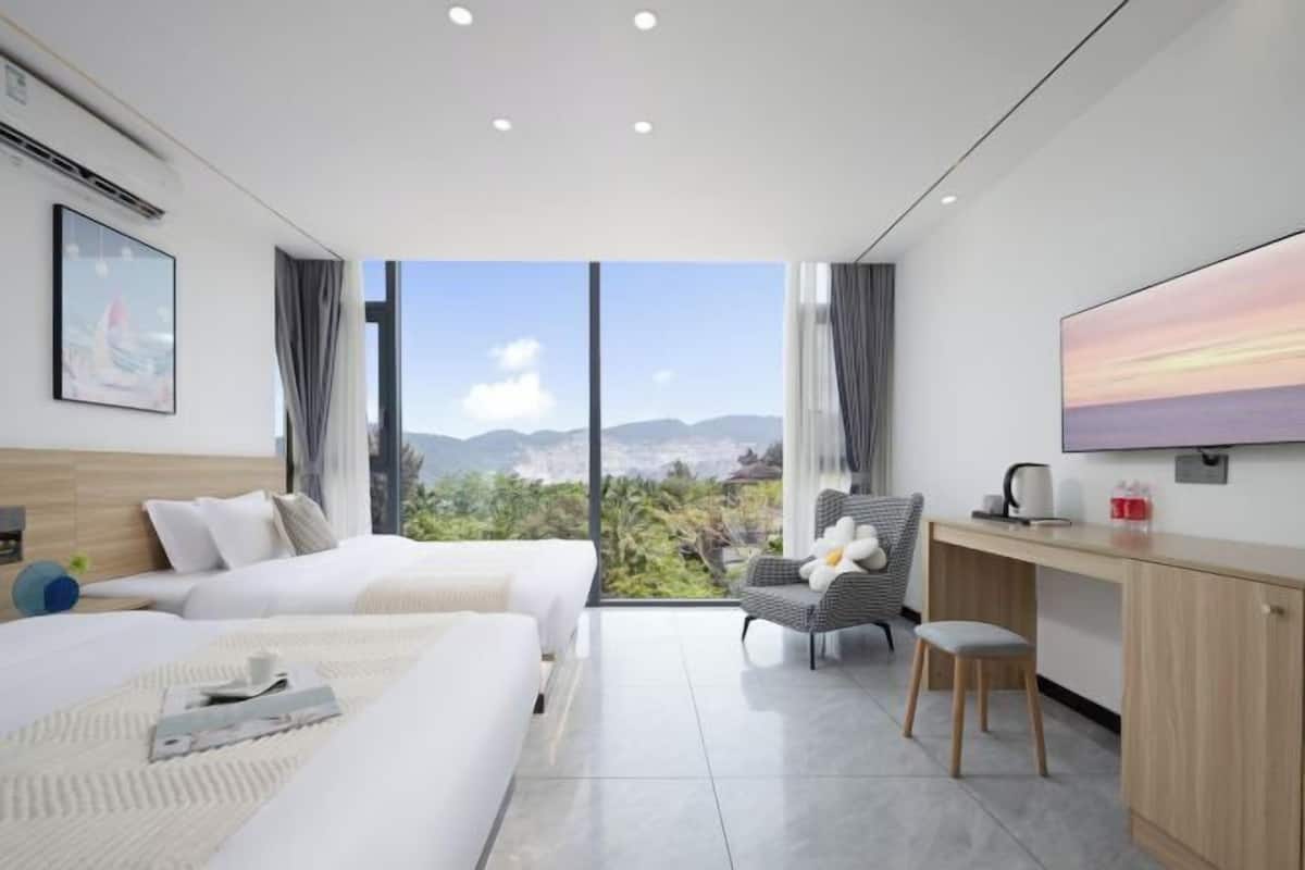 Une chambre d’hôtel moderne équipée de deux lits, d’un bureau, d’une chaise et d’une grande fenêtre donnant sur les montagnes.