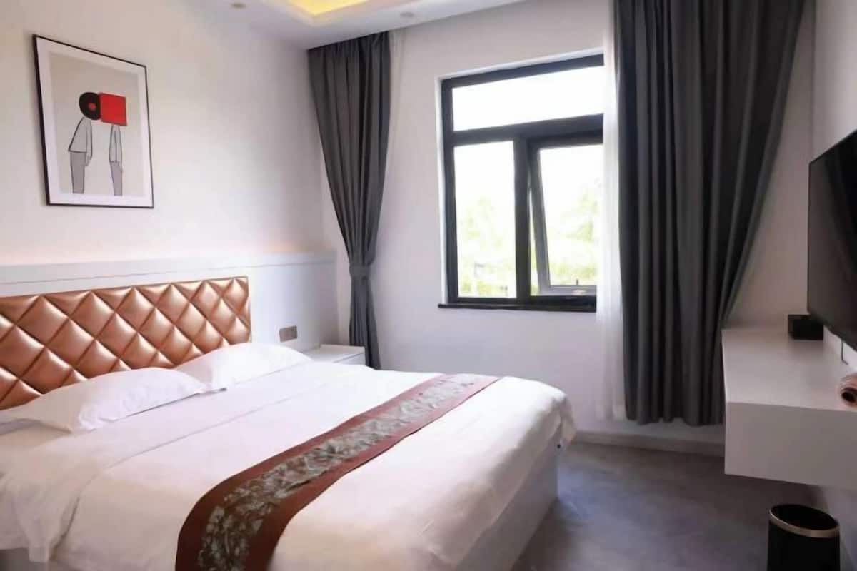 Une chambre d’hôtel avec un lit, une télévision, une fenêtre avec des rideaux et un tableau encadré au mur.